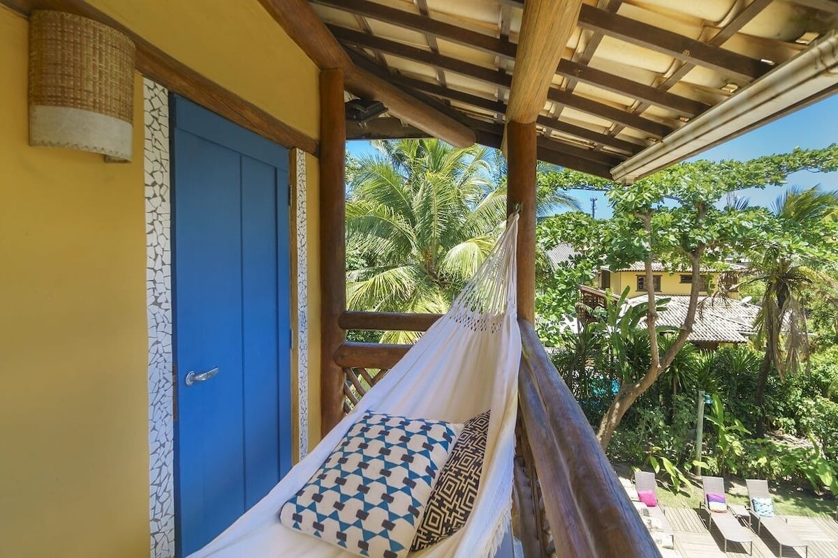 Un hamac agrémenté d’oreillers à motifs, une porte bleue et une vue sur un jardin tropical avec des palmiers.
