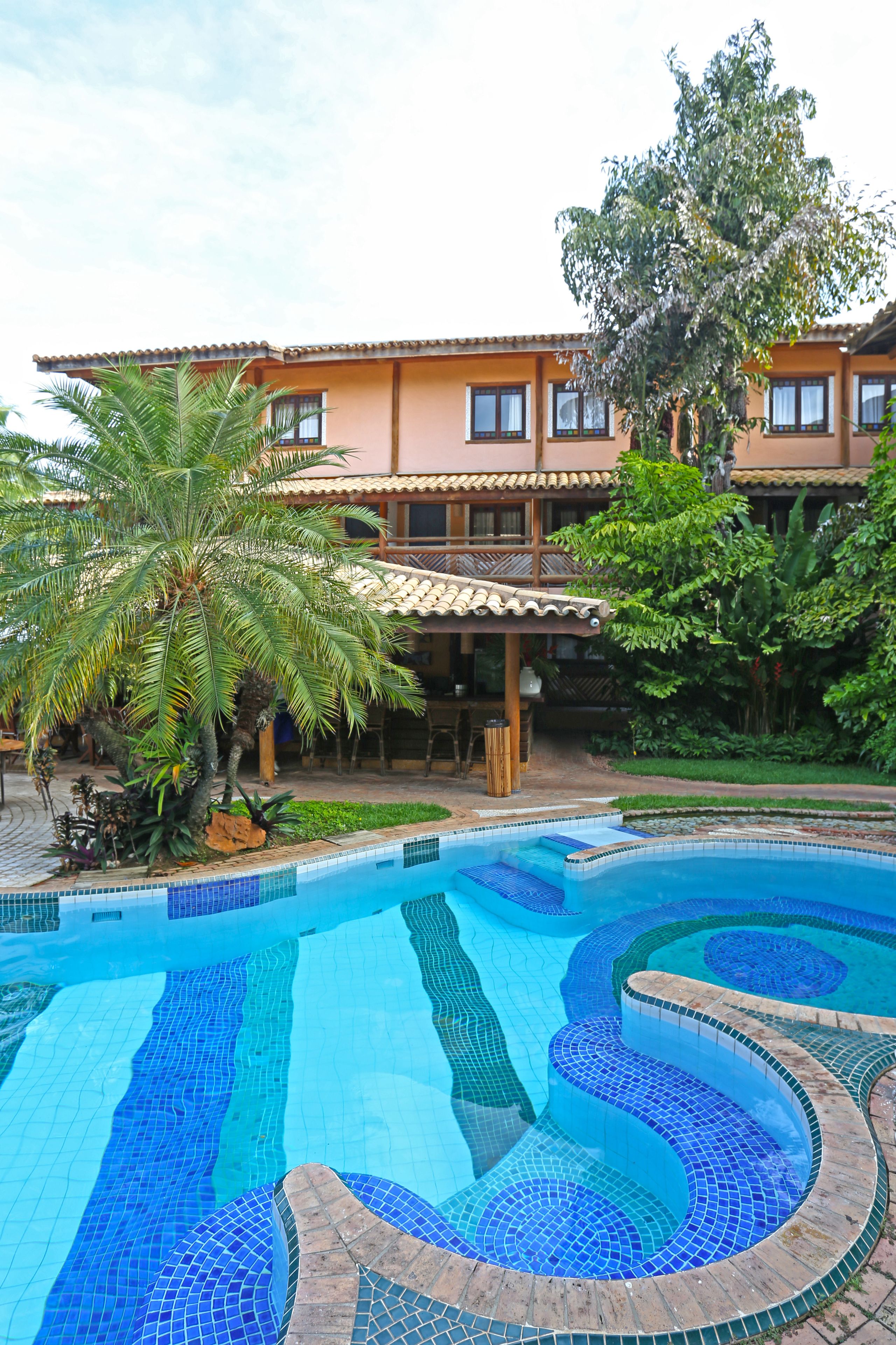 A swimming pool with a tiled design, surrounded by a building with a tiled roof and a palm tree.