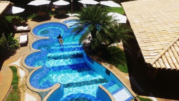 Une piscine à plusieurs niveaux, de forme incurvée, entourée de chaises longues et de parasols.