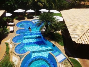 Ein mehrstöckiger Pool mit geschwungener Form, umgeben von Liegestühlen und Sonnenschirmen.