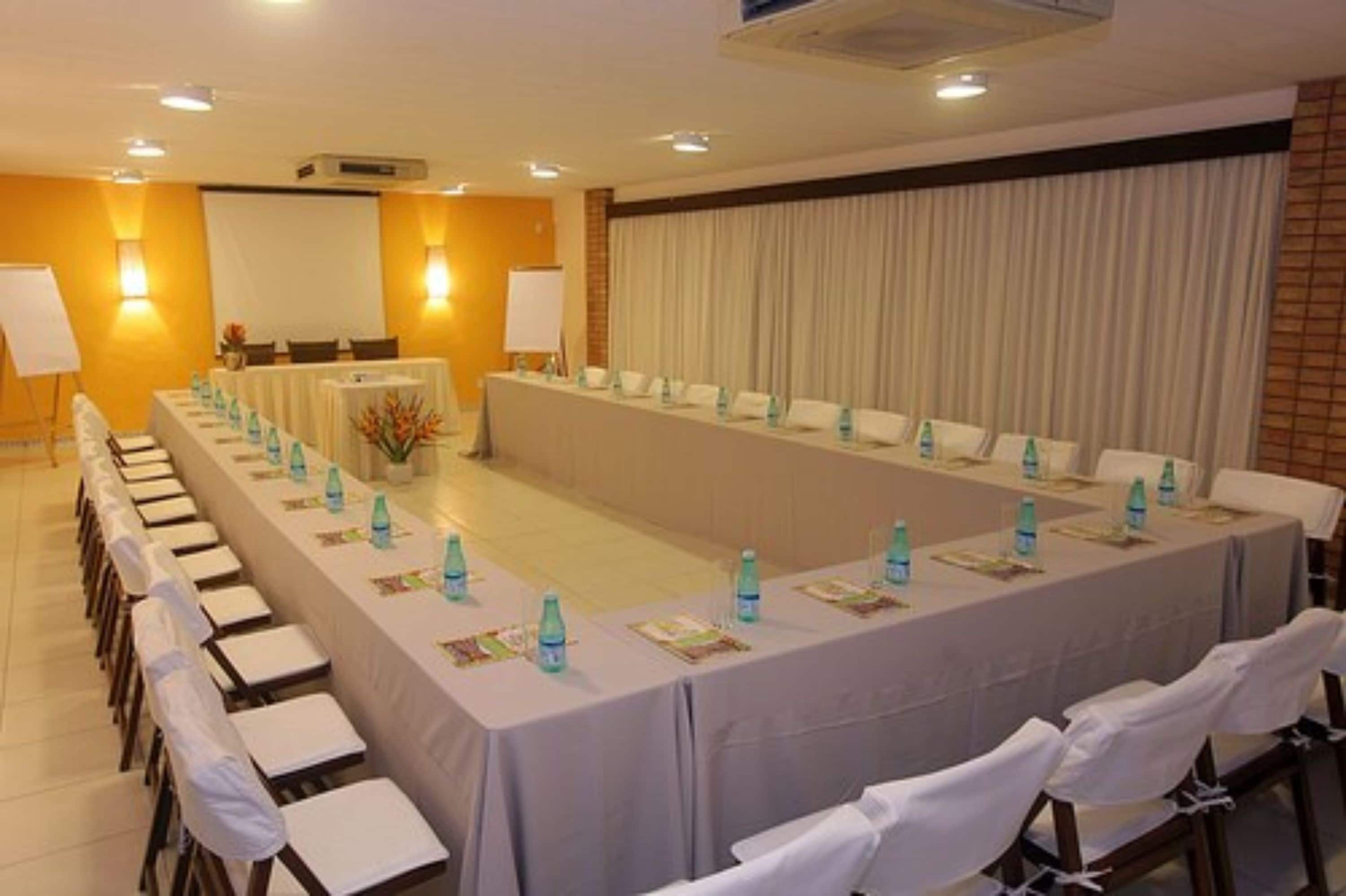 Un salón de conferencias con una larga mesa, sillas y botellas de agua.