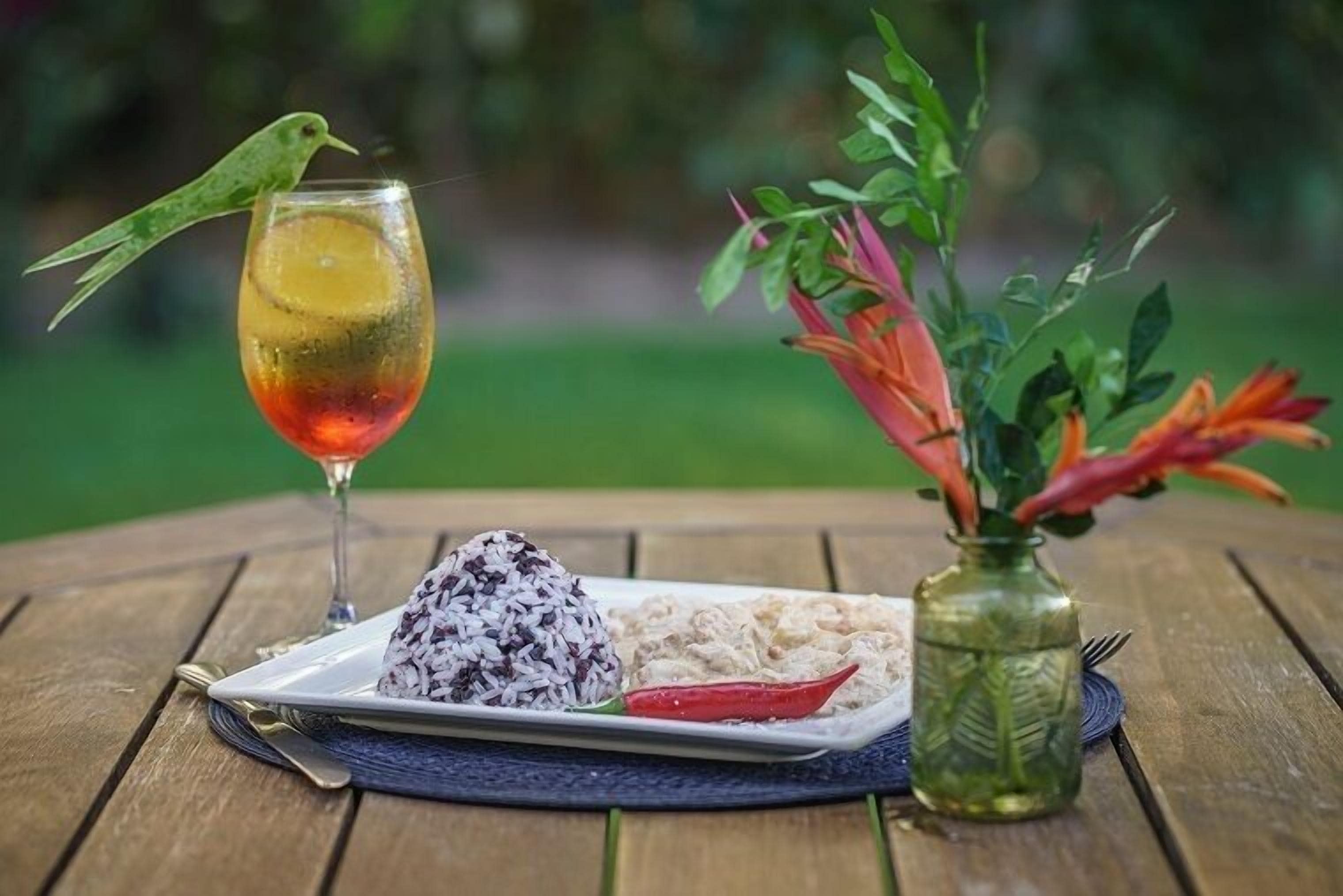 A table with a plate of food, a drink, and a small vase with flowers.