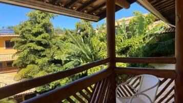 A wooden balcony with white chairs, overlooking a lush garden and a pool.