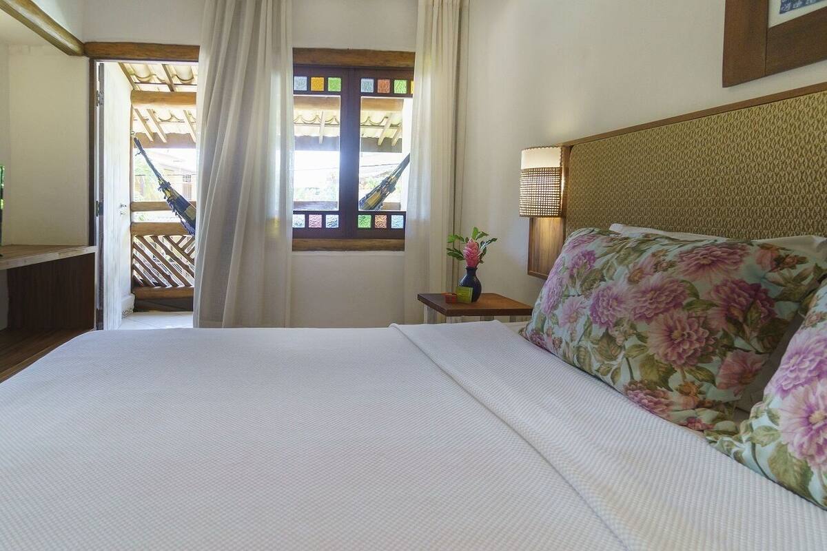 Une chambre d’hôtel avec un lit, une table de chevet avec une lampe, une fenêtre donnant sur un balcon et une porte menant à l’extérieur.