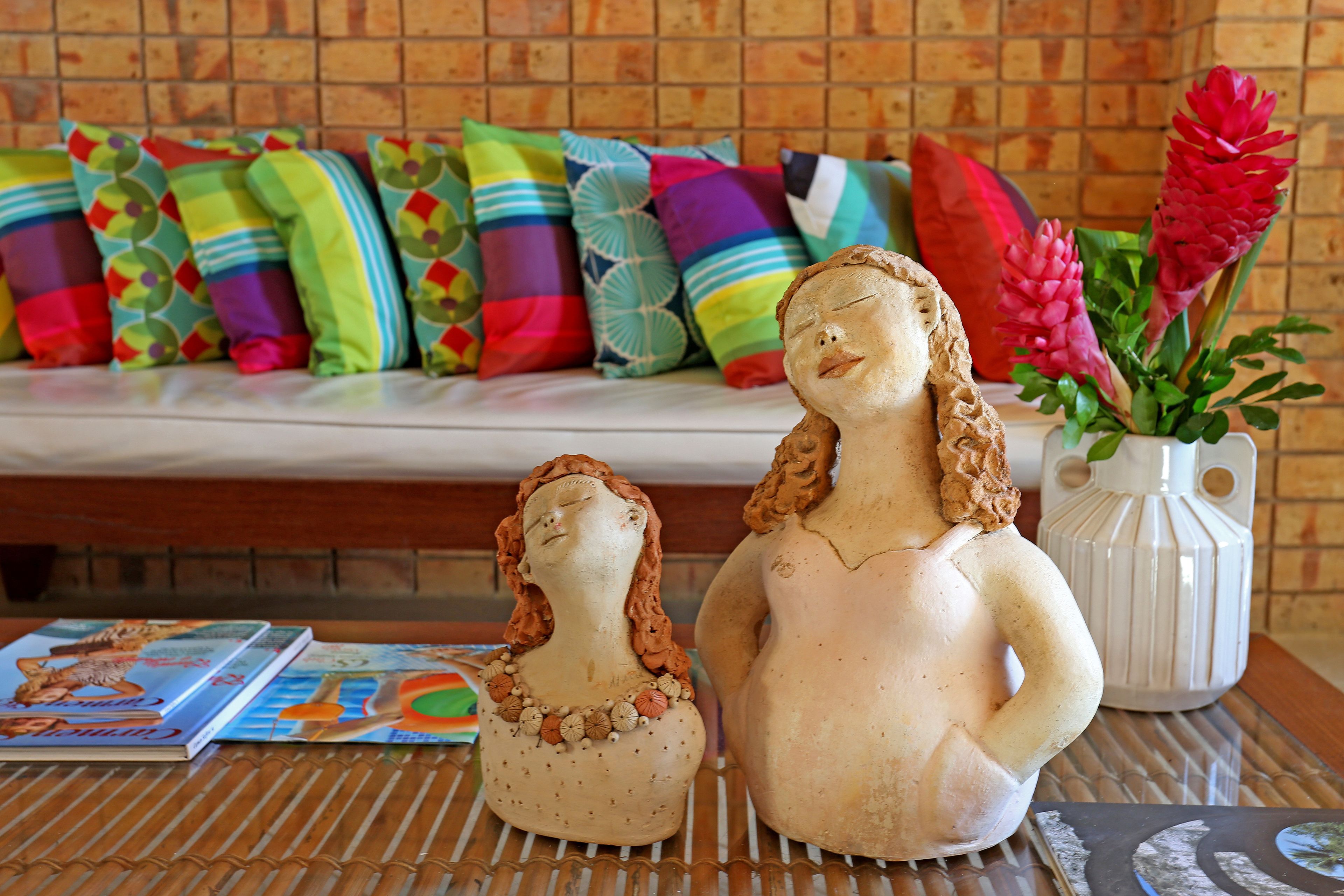 A room with a wooden bench, colorful pillows, and two ceramic figures on a table.