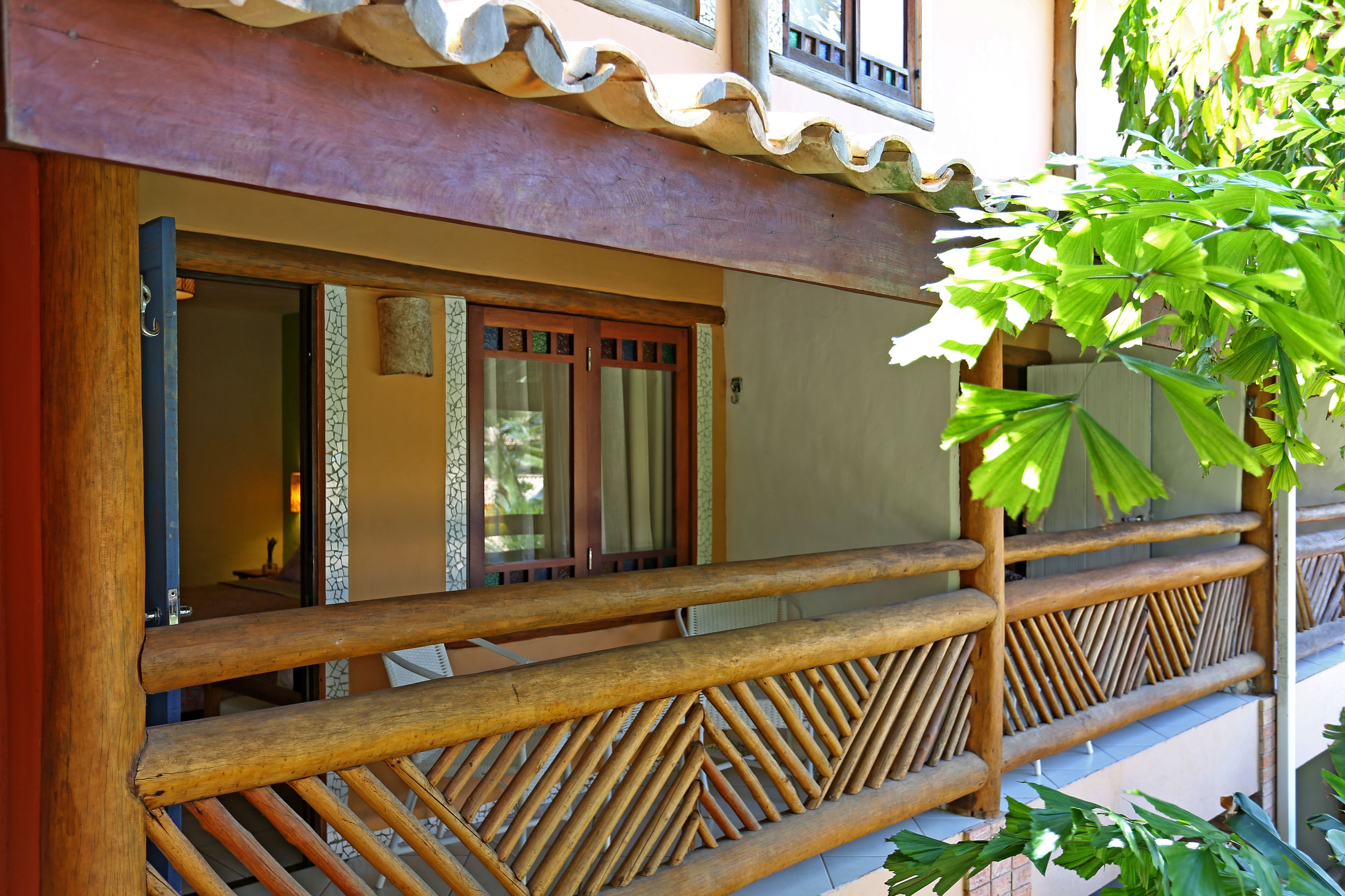 A wooden balcony with a geometric railing design, a tiled roof, and a view of the interior through the open door.