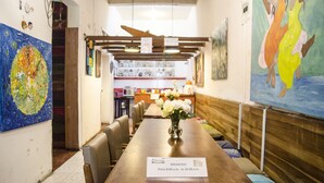 A dining area with a long wooden table, chairs, and a sign indicating breakfast hours. - Hostal Quito Cultural (Quito)