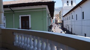 A street view with buildings, a balcony railing, and a distant church tower. - Hostal Quito Cultural (Quito)