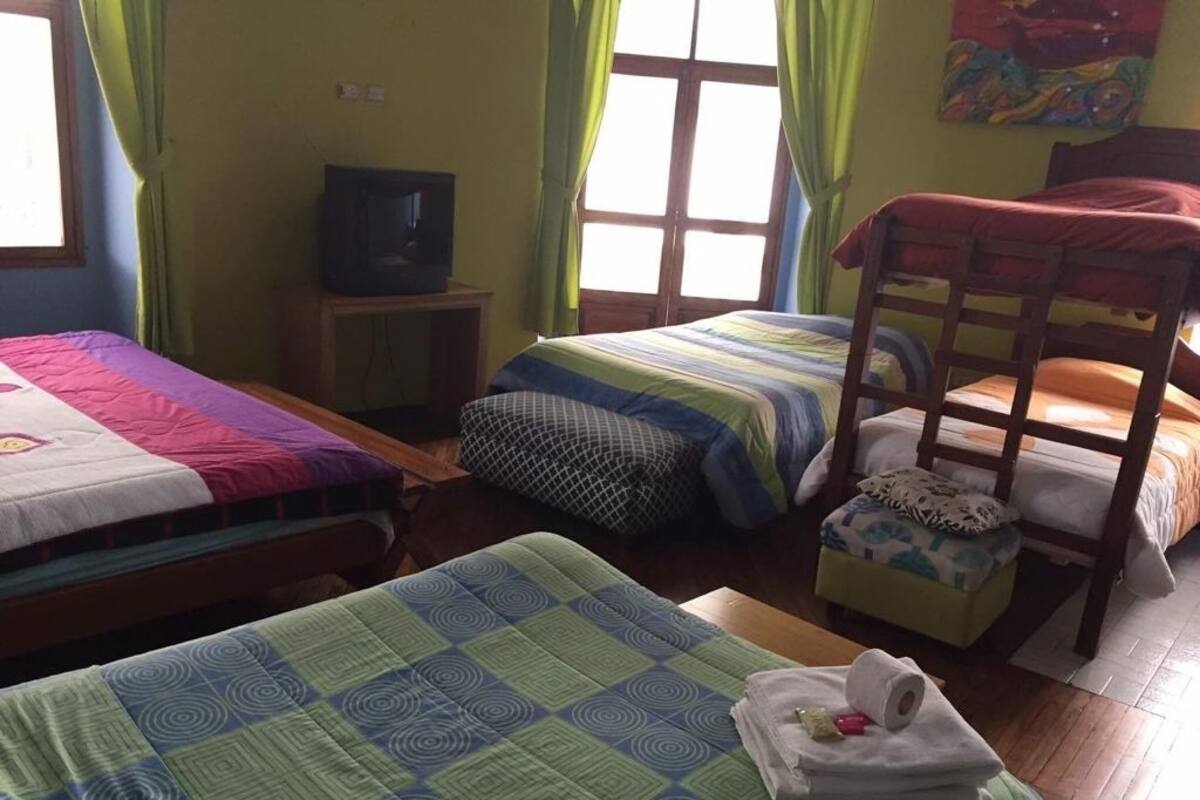 Una habitación con tres camas, televisión y ventana con cortinas.