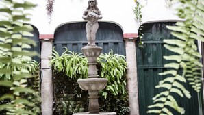 A stone fountain with a statue in a courtyard surrounded by greenery and a building with a red and white facade. - Hostal Quito Cultural (Quito)