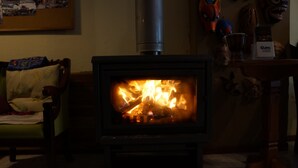 A wood-burning stove with visible flames, a chair with a blanket, and a table with decorative items. - Hostal Quito Cultural (Quito)
