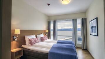 Une chambre d’hôtel avec un grand lit, une table de chevet, une lampe, une fenêtre avec des rideaux et un tableau encadré au mur.