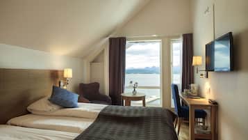 Habitación de hotel con dos camas, un escritorio con silla, televisión y vista al mar.