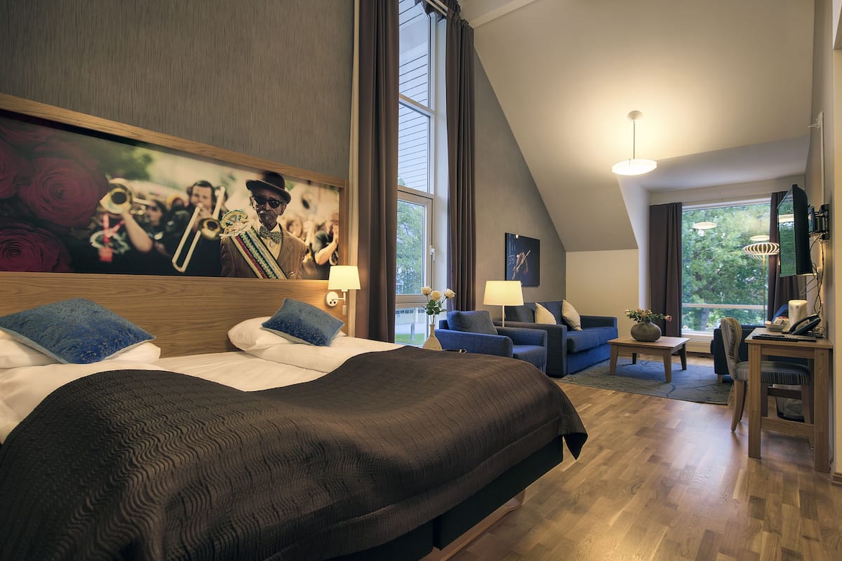 A modern hotel room with a large bed, two sofas, a desk, and a painting of musicians.