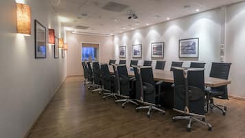 Un salón de conferencias con una mesa larga, sillas, cuadros en la pared y piso de madera.