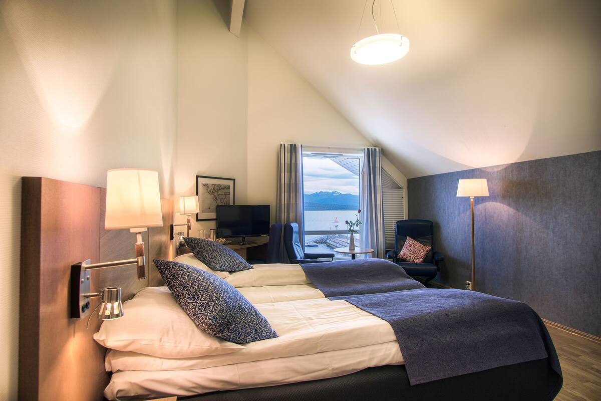 A hotel room with two beds, a desk with a computer, a TV, and a view of the outdoors.