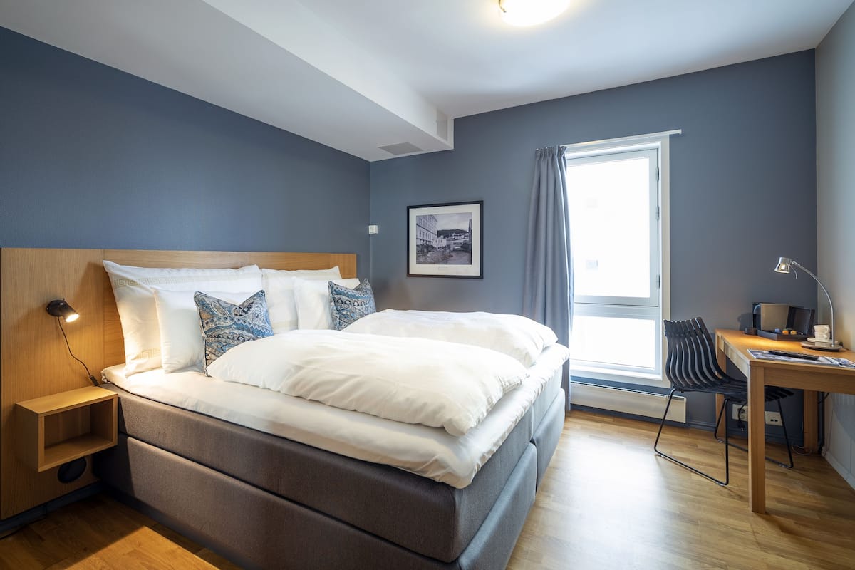 A modern bedroom with a large bed, a desk with a chair, and a window with curtains.