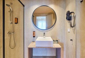 Une salle de bain moderne avec un grand miroir, un lavabo, une douche et un sèche-cheveux fixé au mur.