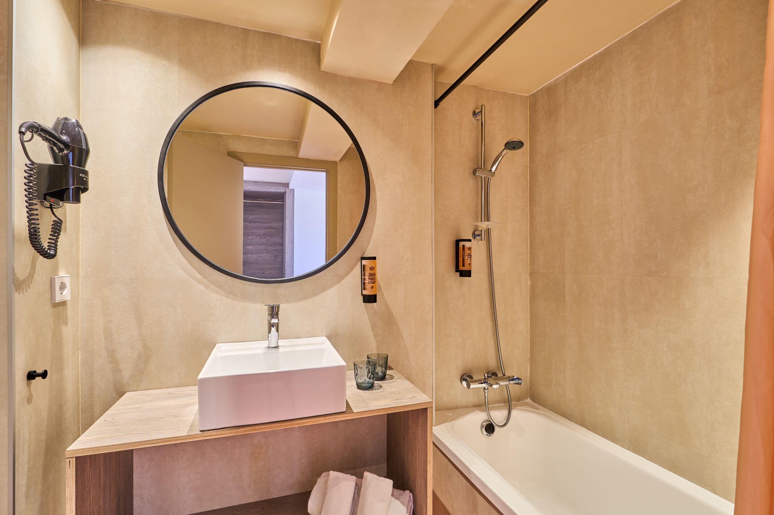 Een badkamer met een ronde spiegel, een wastafel, een handdouche en een bad.