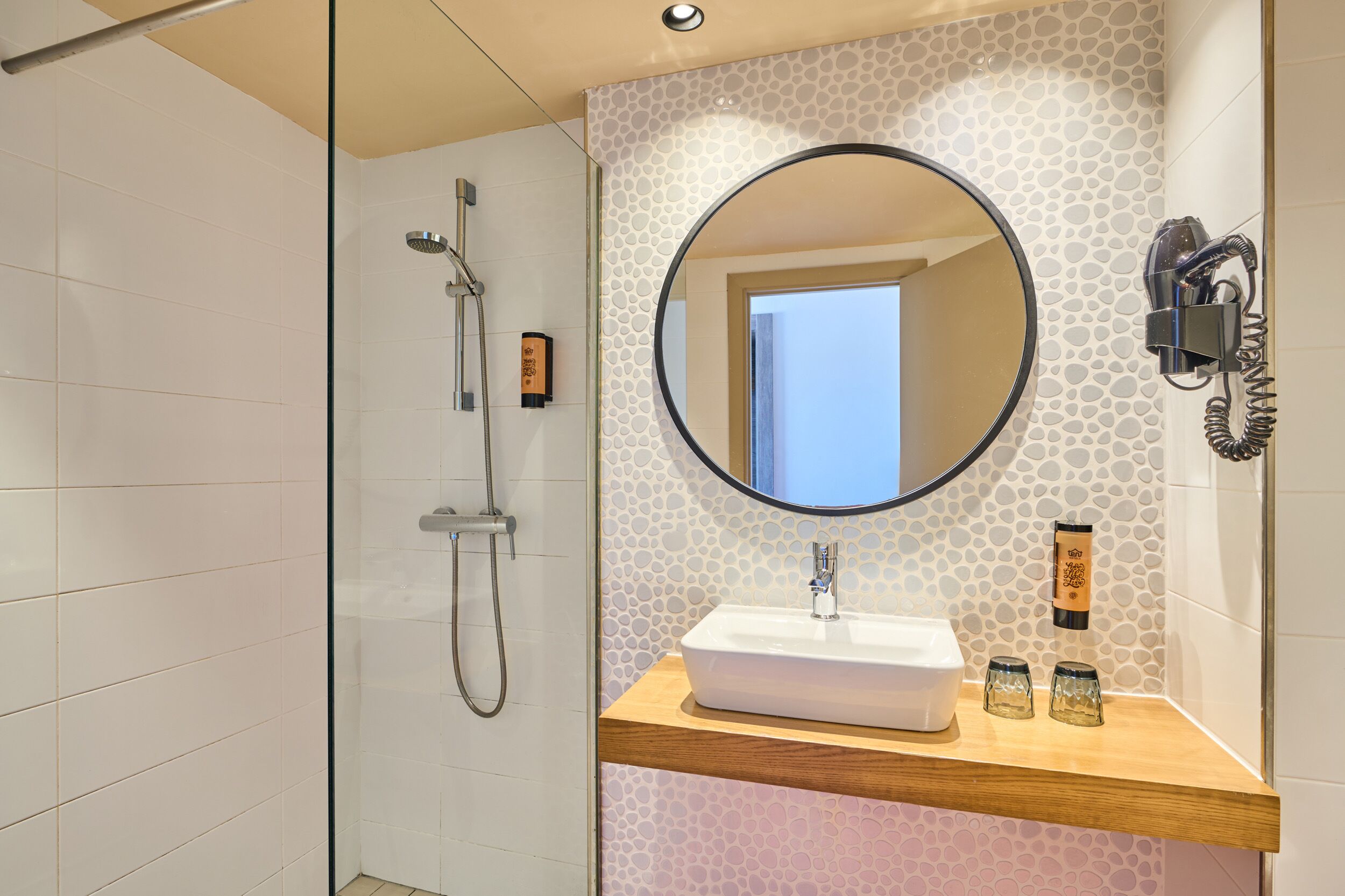 A modern bathroom with a shower, a sink with a mirror, and a hairdryer mounted on the wall.