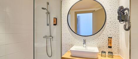 A modern bathroom with a shower, a sink with a mirror, and a hairdryer mounted on the wall.