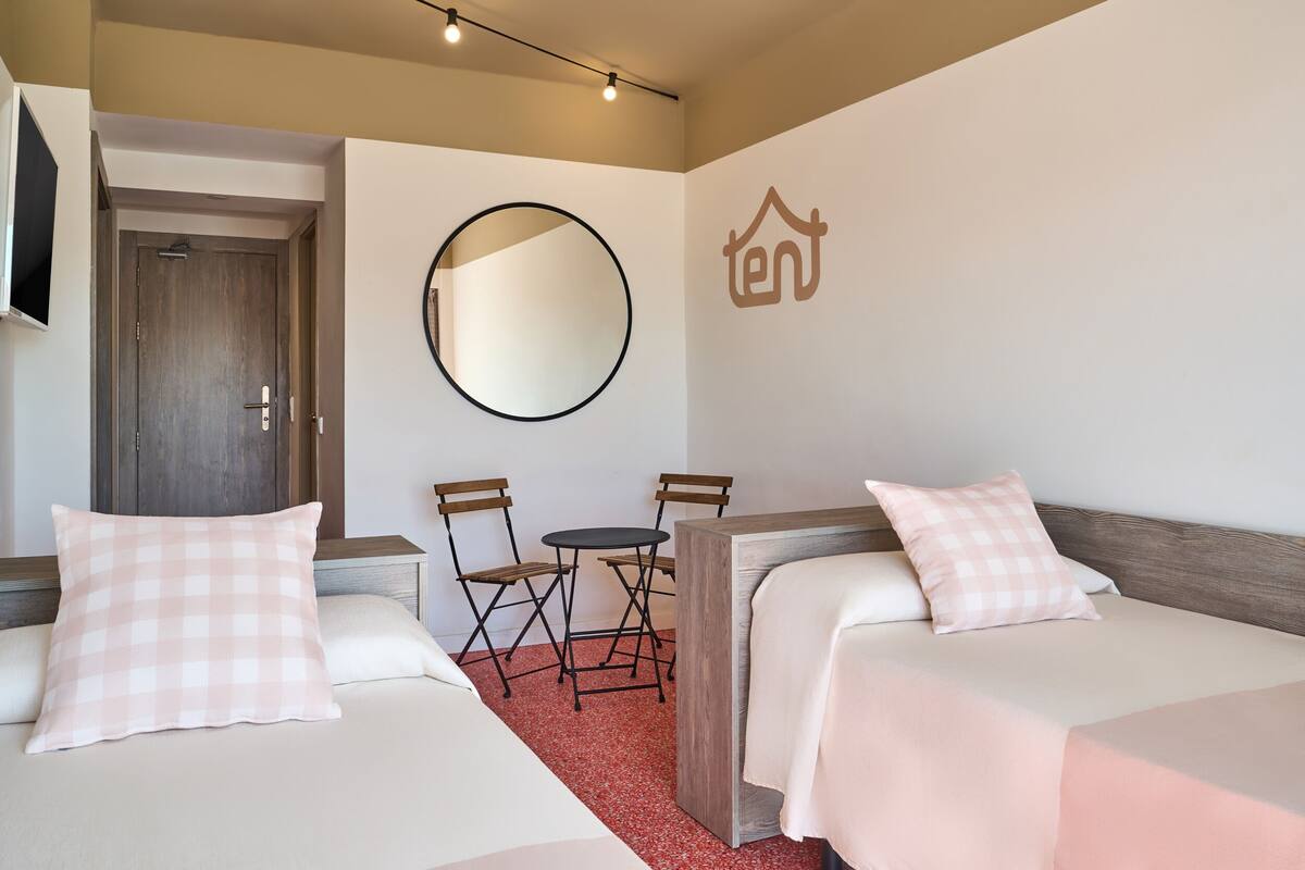 A hotel room with two beds, a round mirror, a small table, and a TV on the wall.