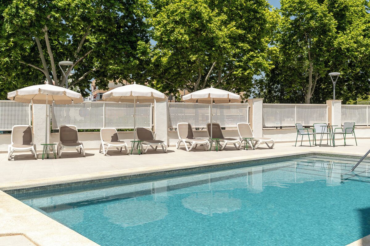 A swimming pool with lounge chairs and umbrellas, surrounded by a fence and trees.
