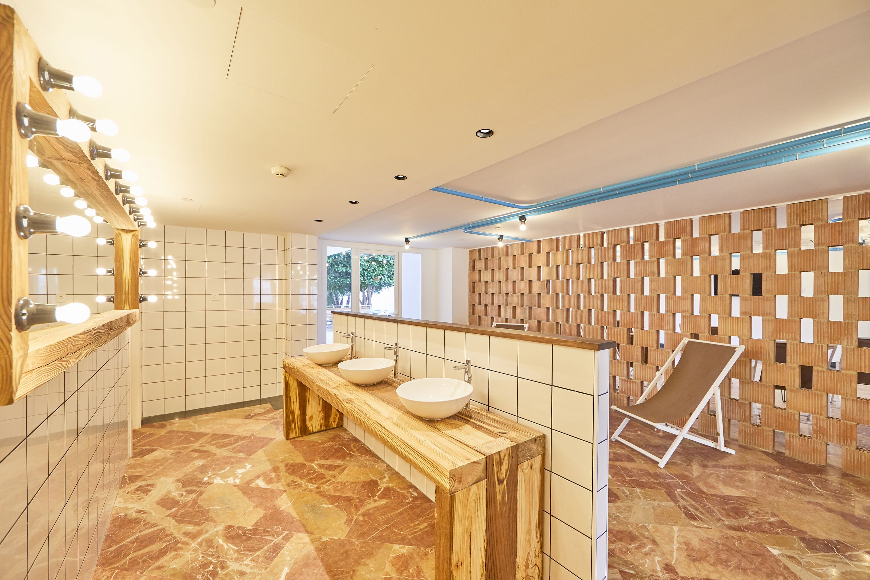 Un baño moderno con tres lavamanos, un mueble de tocador de madera y un espejo grande con iluminación.