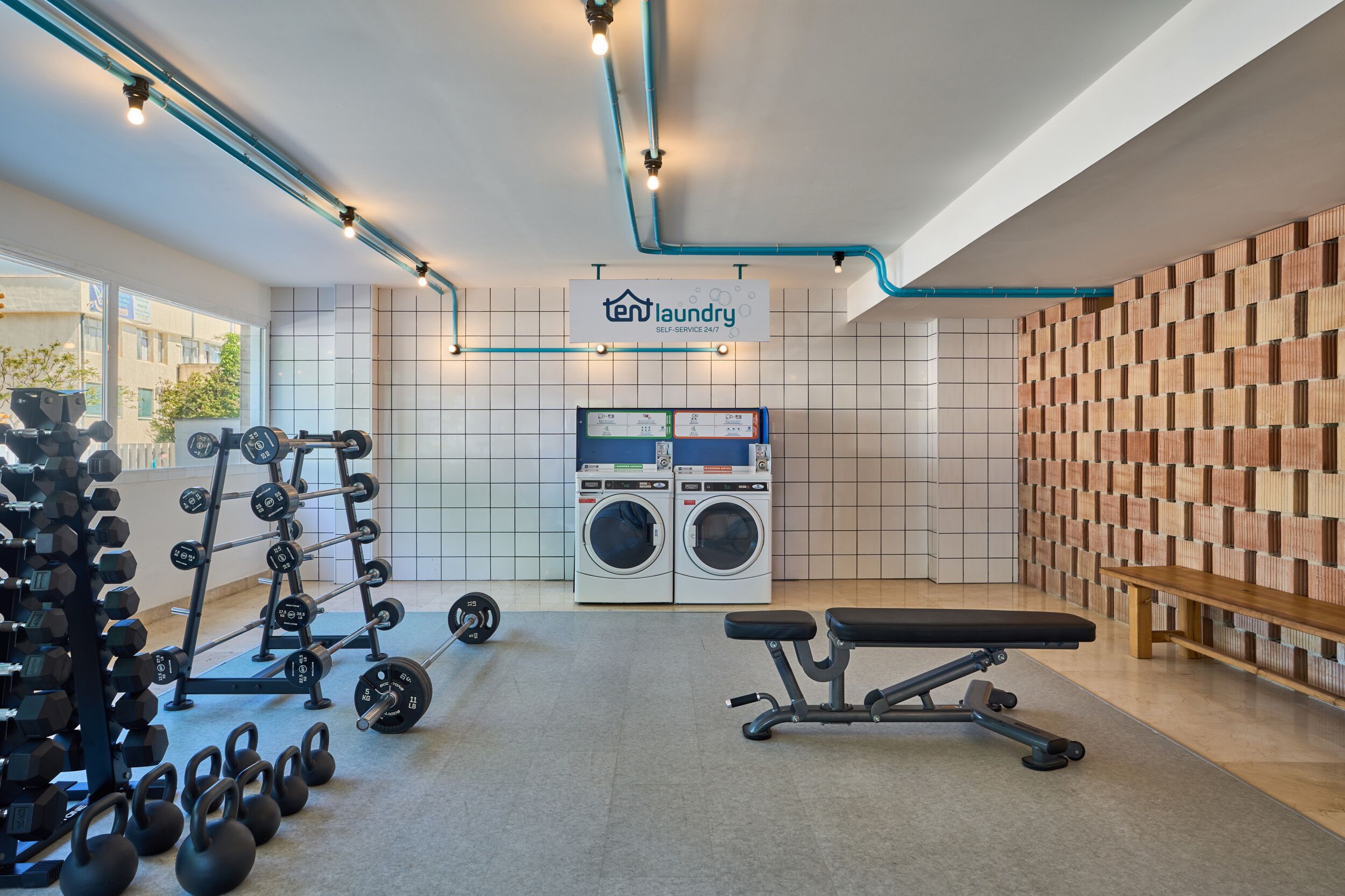 A gym with weightlifting equipment, a bench, and a sign for 'ten laundry self-service 24/7'.