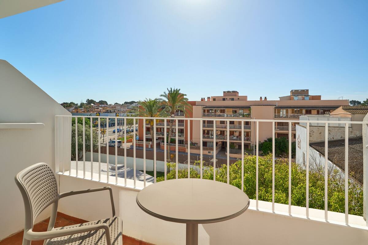 A balcony with a chair and table, overlooking a residential area with buildings and a street.