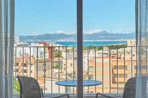 En balkon med bord og stole, der ud til et kystlandskab med bygninger og bjerge.