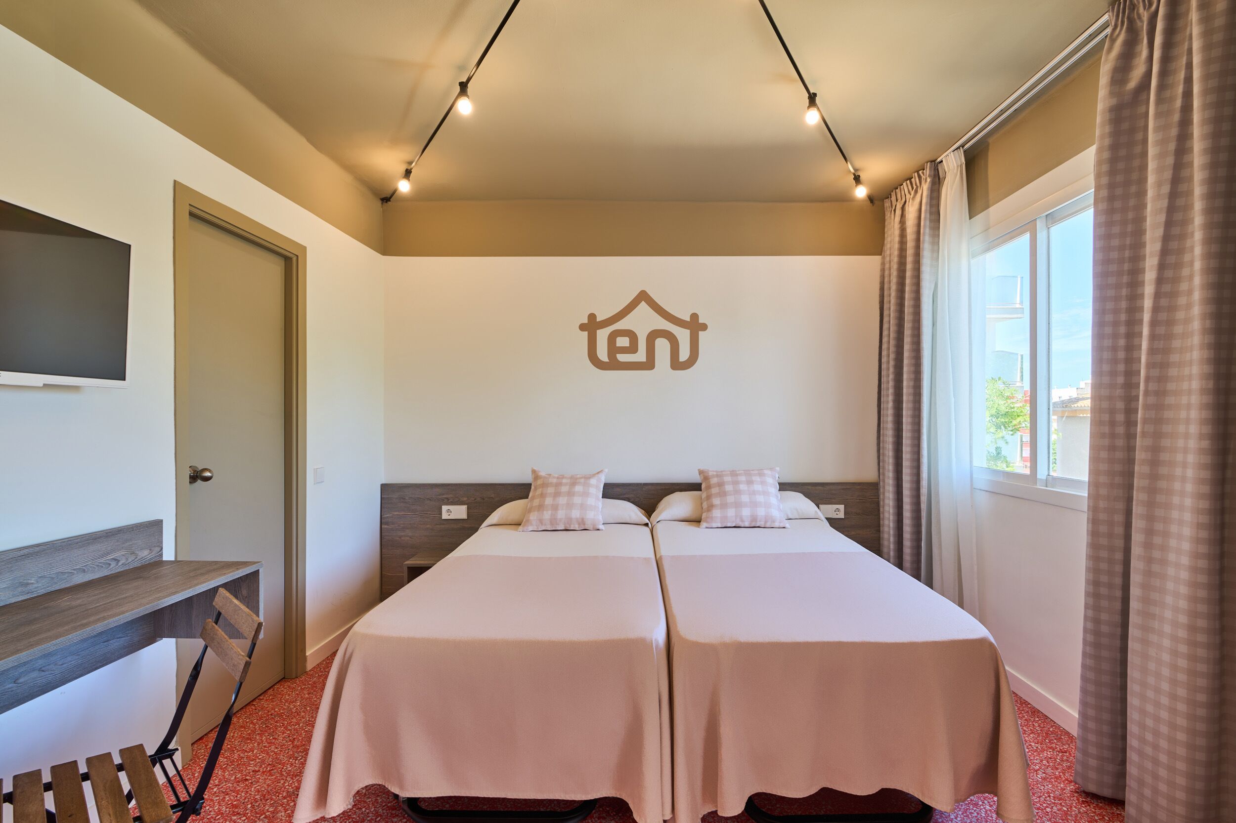 Une chambre d’hôtel avec deux lits, un téléviseur fixé au mur, un bureau et une fenêtre avec des rideaux.