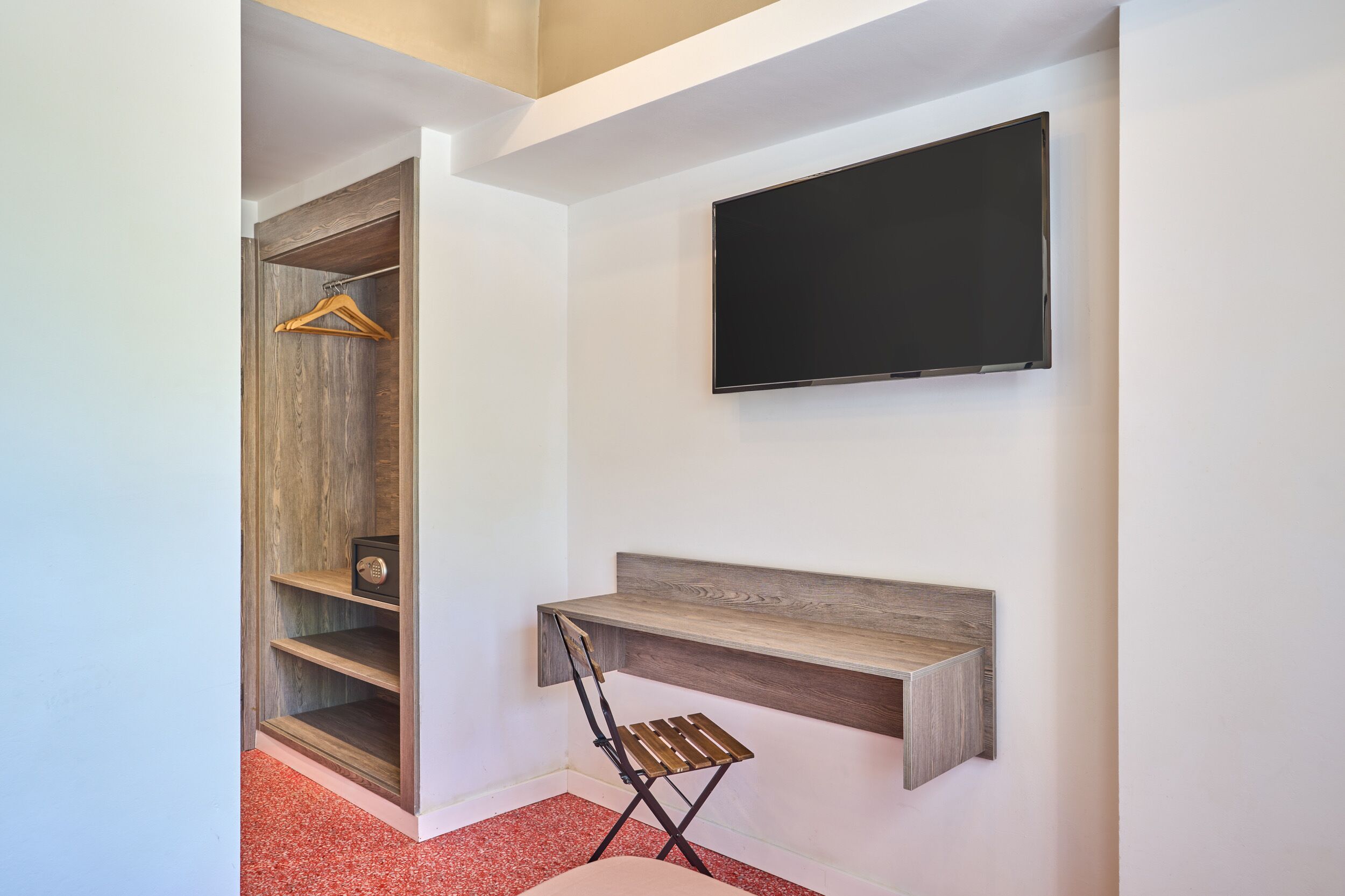 A room with a wooden wardrobe, a mounted TV, and a foldable desk.
