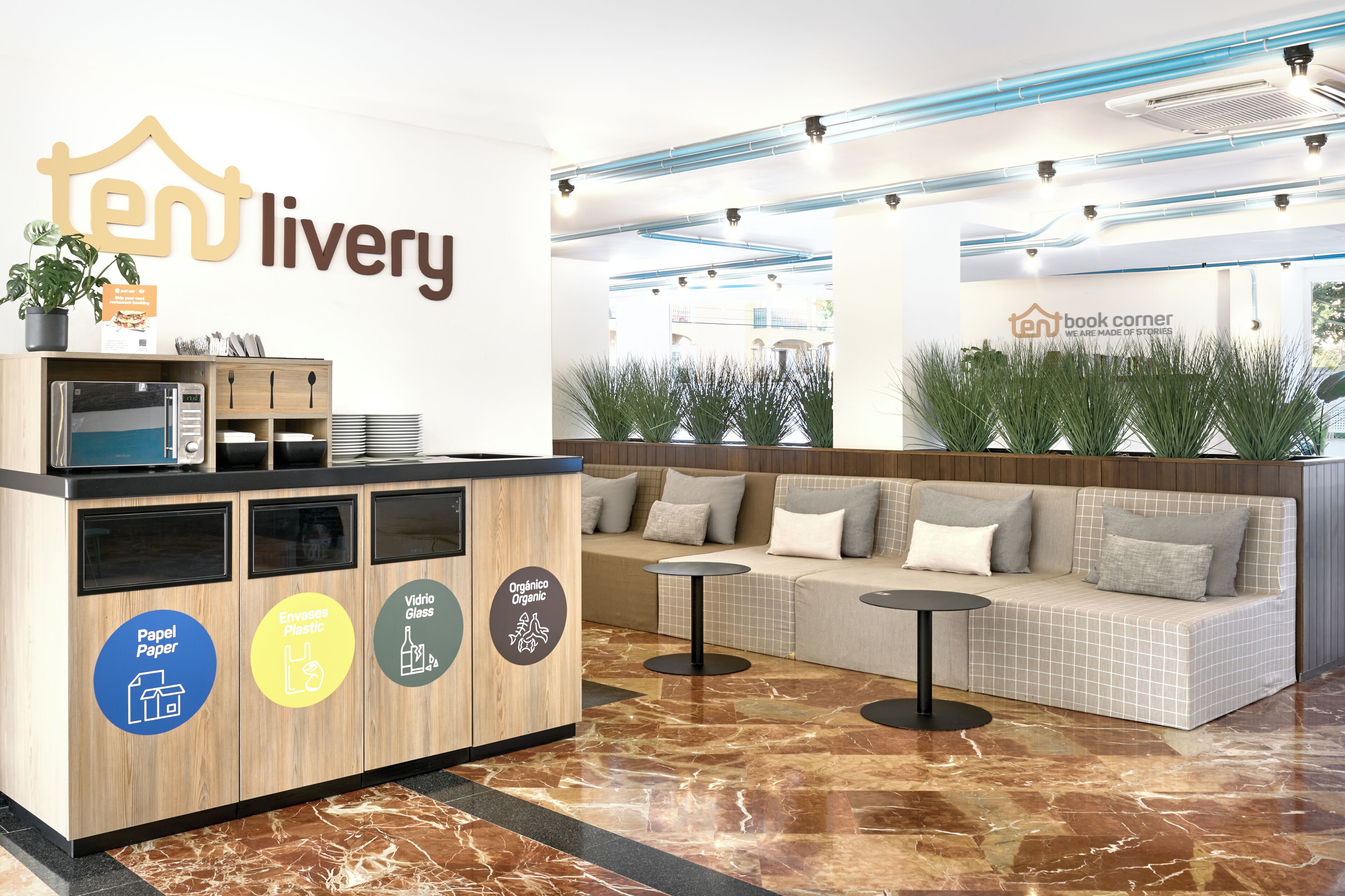 A reception area with a wooden counter, recycling bins, a seating area with a sofa and tables, and a wall with signage.