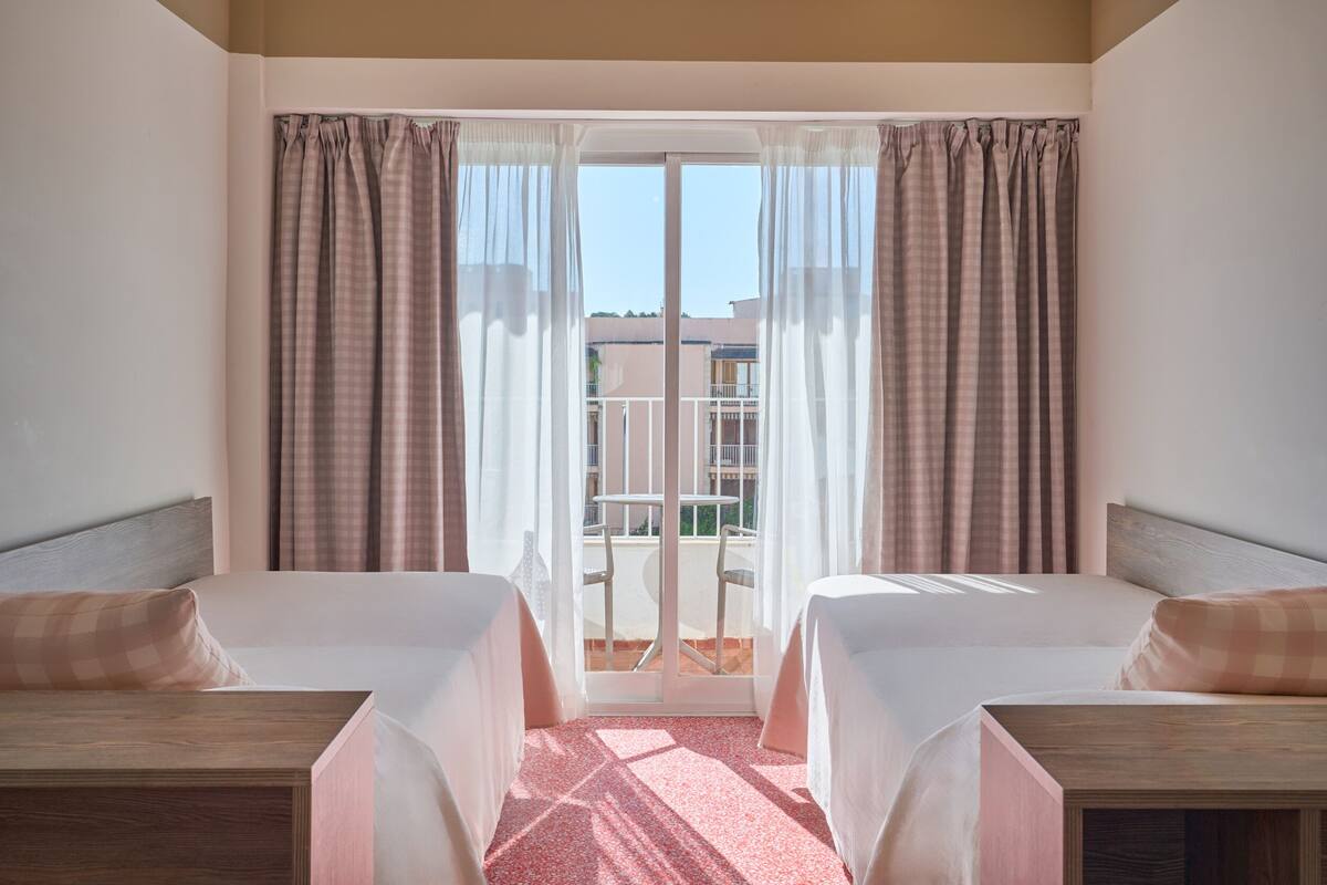 A hotel room with two beds, a balcony, and a view of buildings.