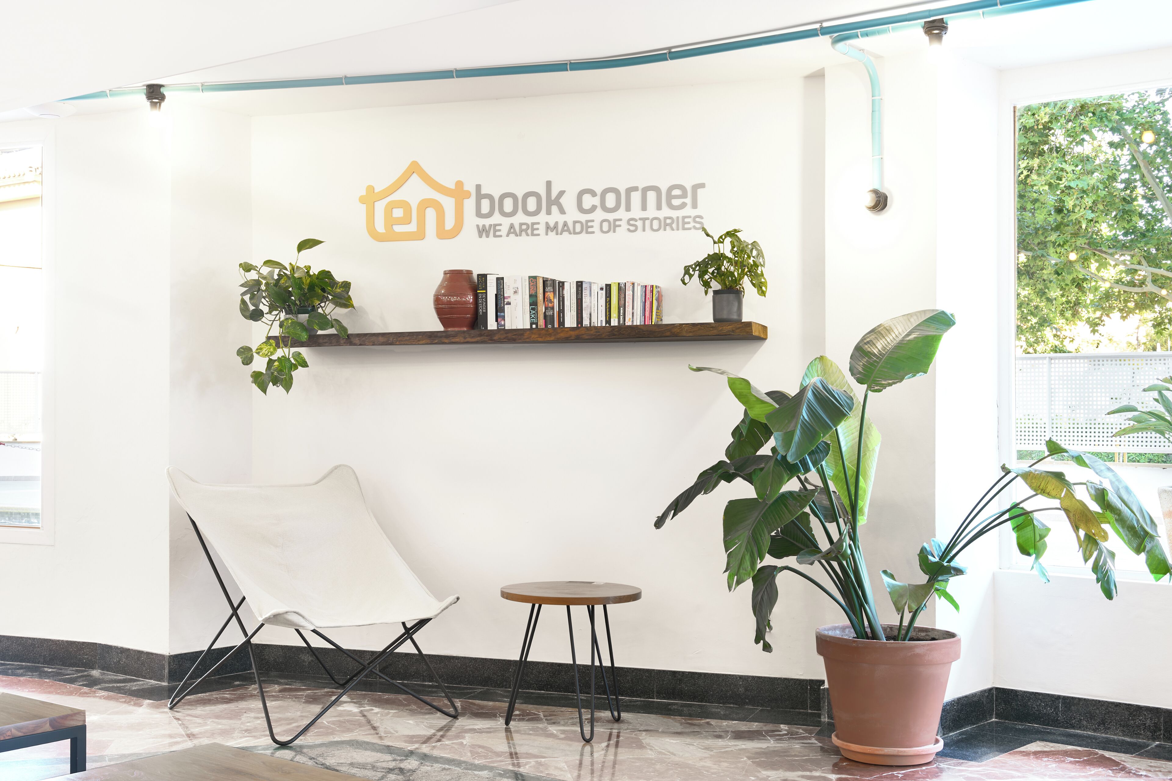 Un coin lecture avec un fauteuil, une petite table et une bibliothèque contenant des livres et des plantes.