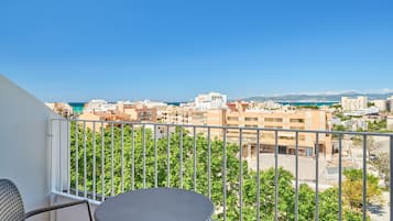 Un balcone con tavolo e sedie, affaccia su un panorama urbano con edifici e cielo sereno.