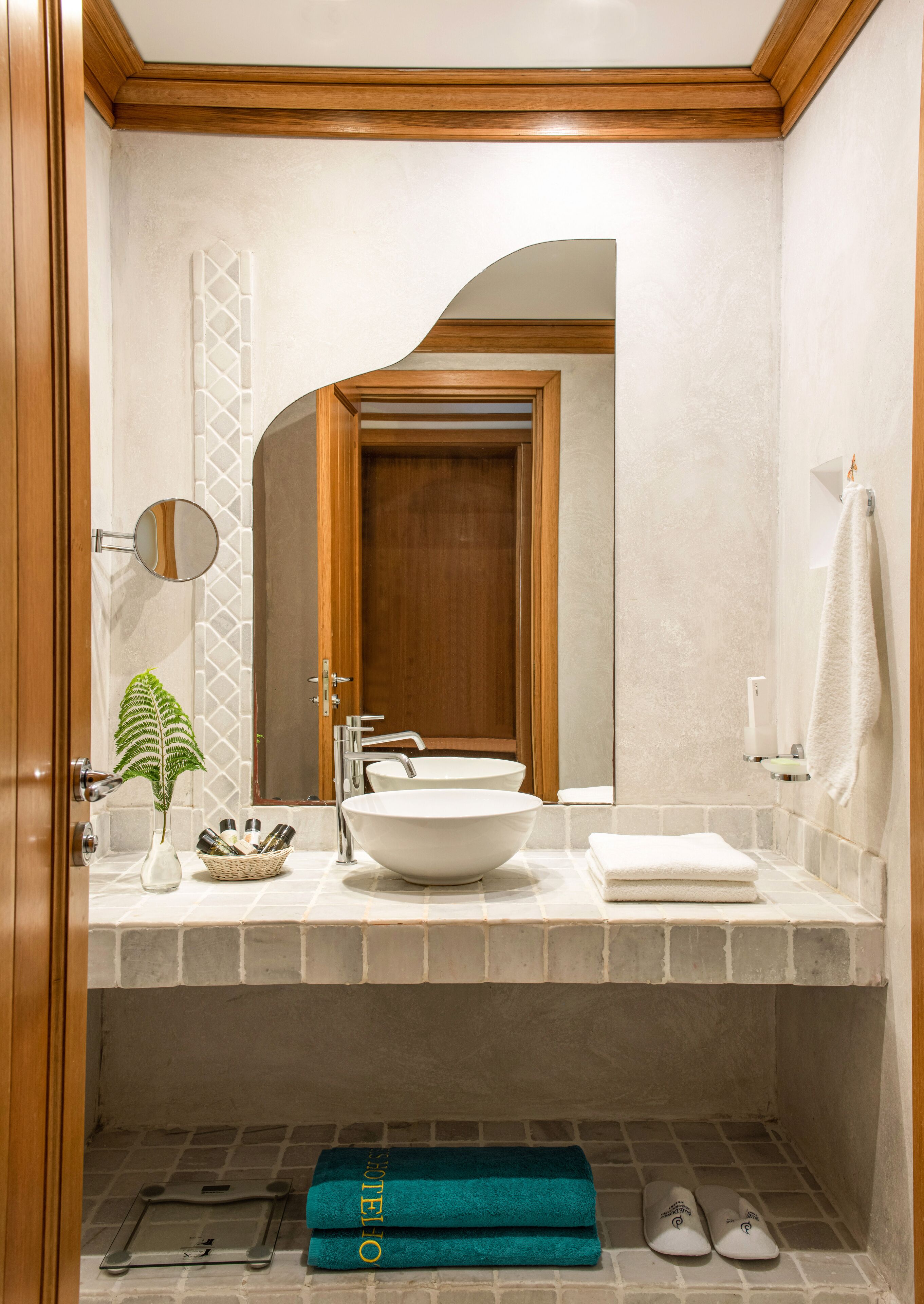 Une salle de bain avec une porte en bois, un lavabo blanc, un miroir, un porte-serviettes et une serviette accrochée au mur.