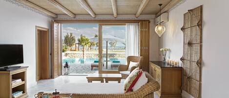 A spacious room with a large bed, a wicker sofa, a TV, and a view of a pool and palm trees.
