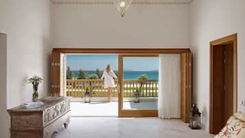 A spacious room with a balcony overlooking the sea, a wooden dresser, and a bed with a book on it.