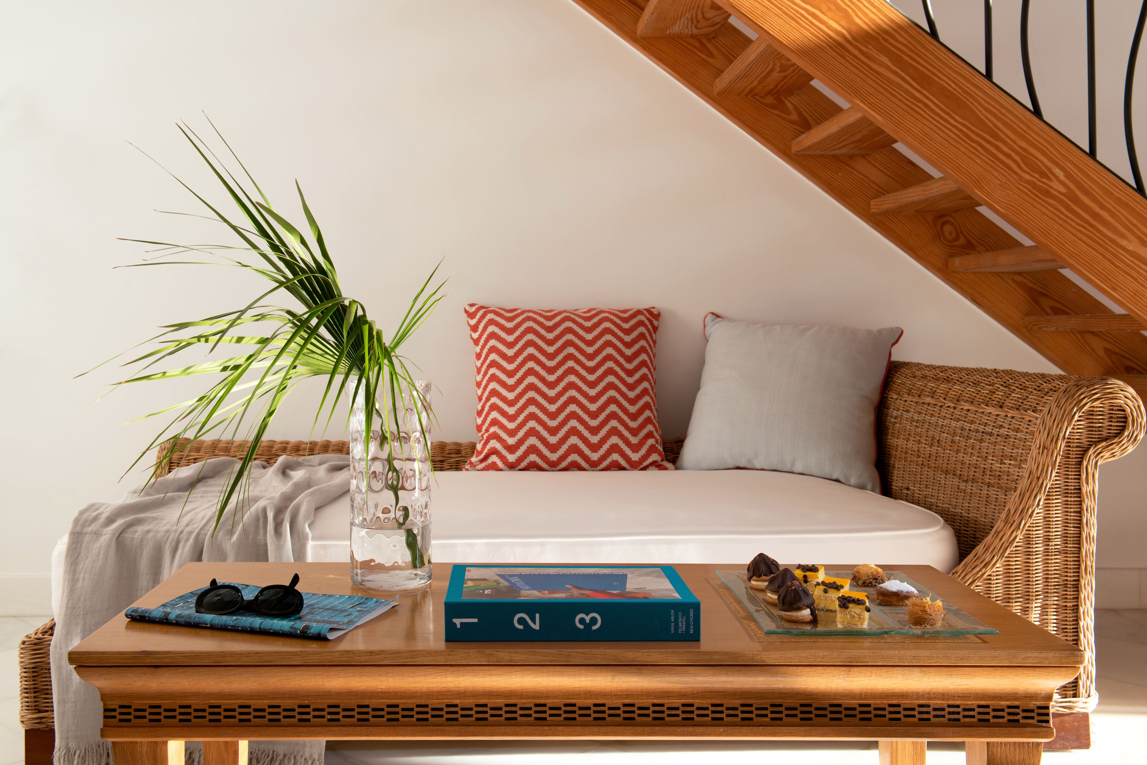 Una habitación acogedora con una mesa de madera, un sofá de mimbre, una cama blanca y un cojín rojo y blanco.