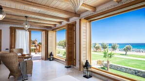 Amplia habitación con un gran ventanal que ofrece vistas al mar, muebles de mimbre y un techo con vigas de madera.