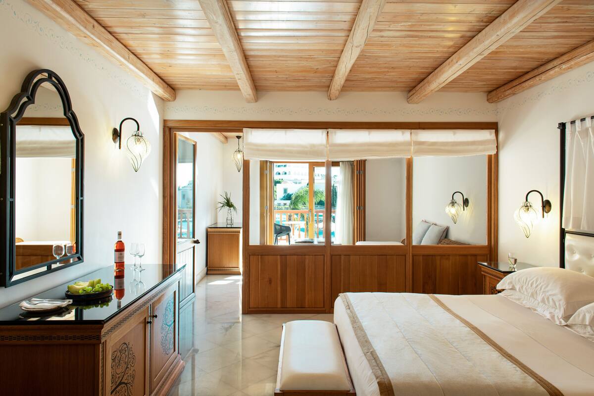 Ein Schlafzimmer mit einem großen Bett, Holzbalkendecke, einem Schminktisch und einem Fenster mit Blick ins Freie.