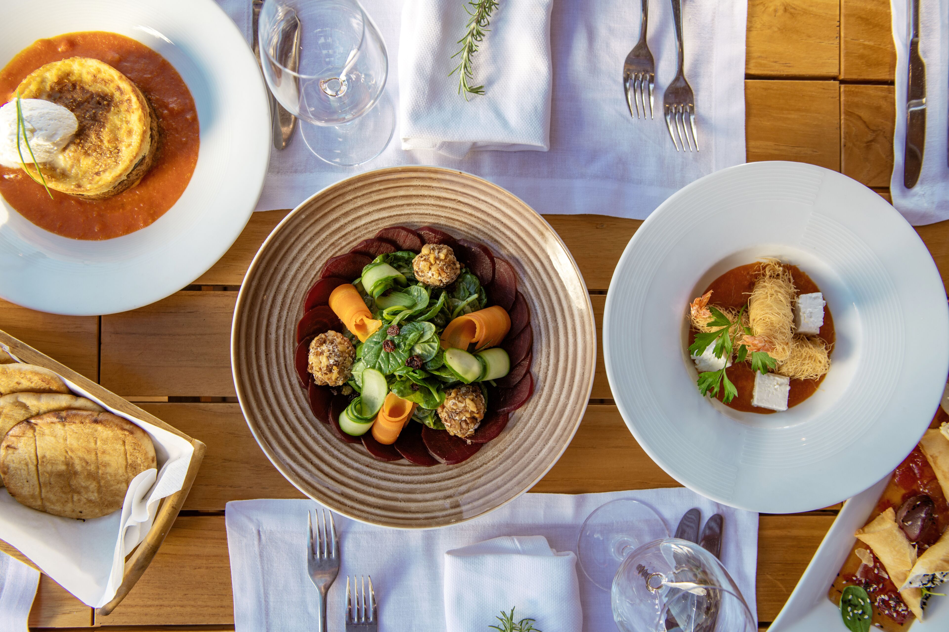 A dining table with various dishes, including a bowl of salad, a plate of meatballs, and a bowl of soup. There are also wine glasses and cutlery on the table.