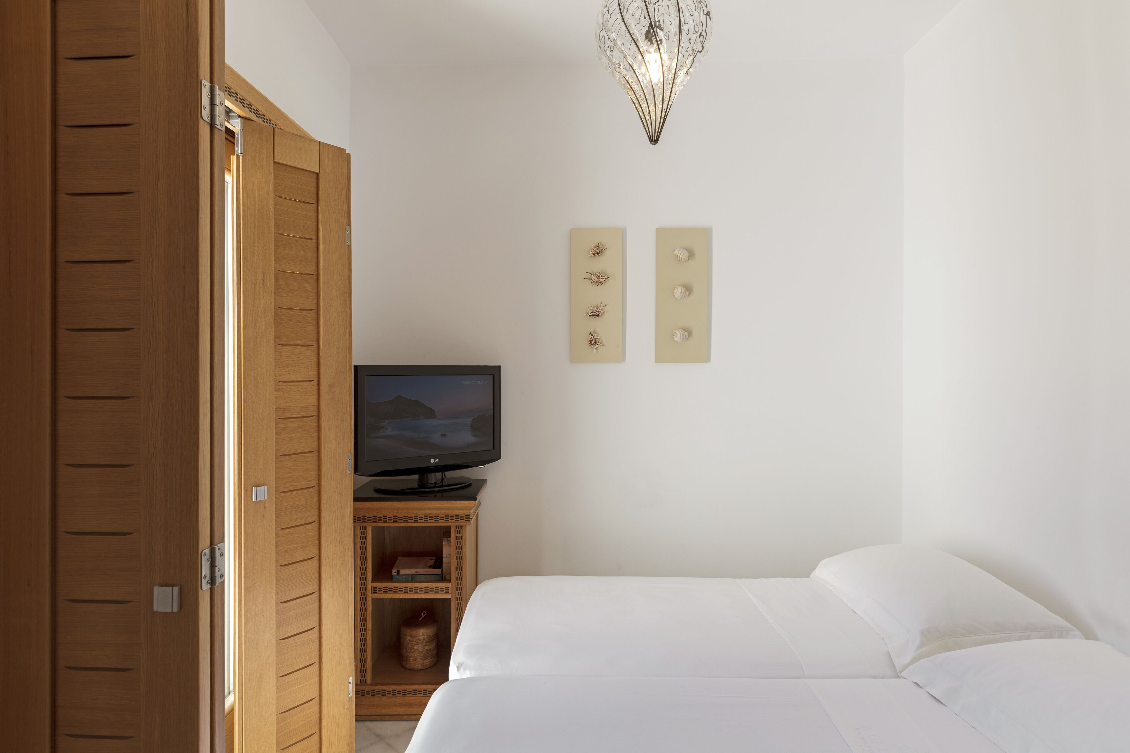 Un dormitorio con cama, televisión sobre un mueble de madera y armario.