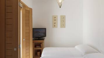 Un dormitorio con cama, televisión sobre un mueble de madera y armario.