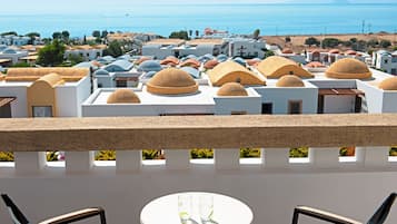 A terrace with a table and chairs, overlooking a coastal town with white buildings and domed roofs.
