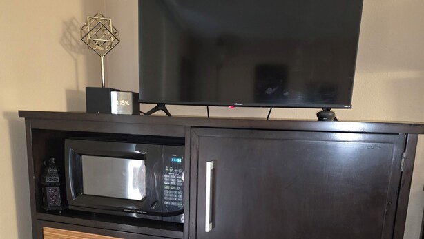 A dark wooden cabinet with a microwave, a flat-screen TV on top, and two drawers. - Monroe Motel Near Seattle Everett WA (Monroe)