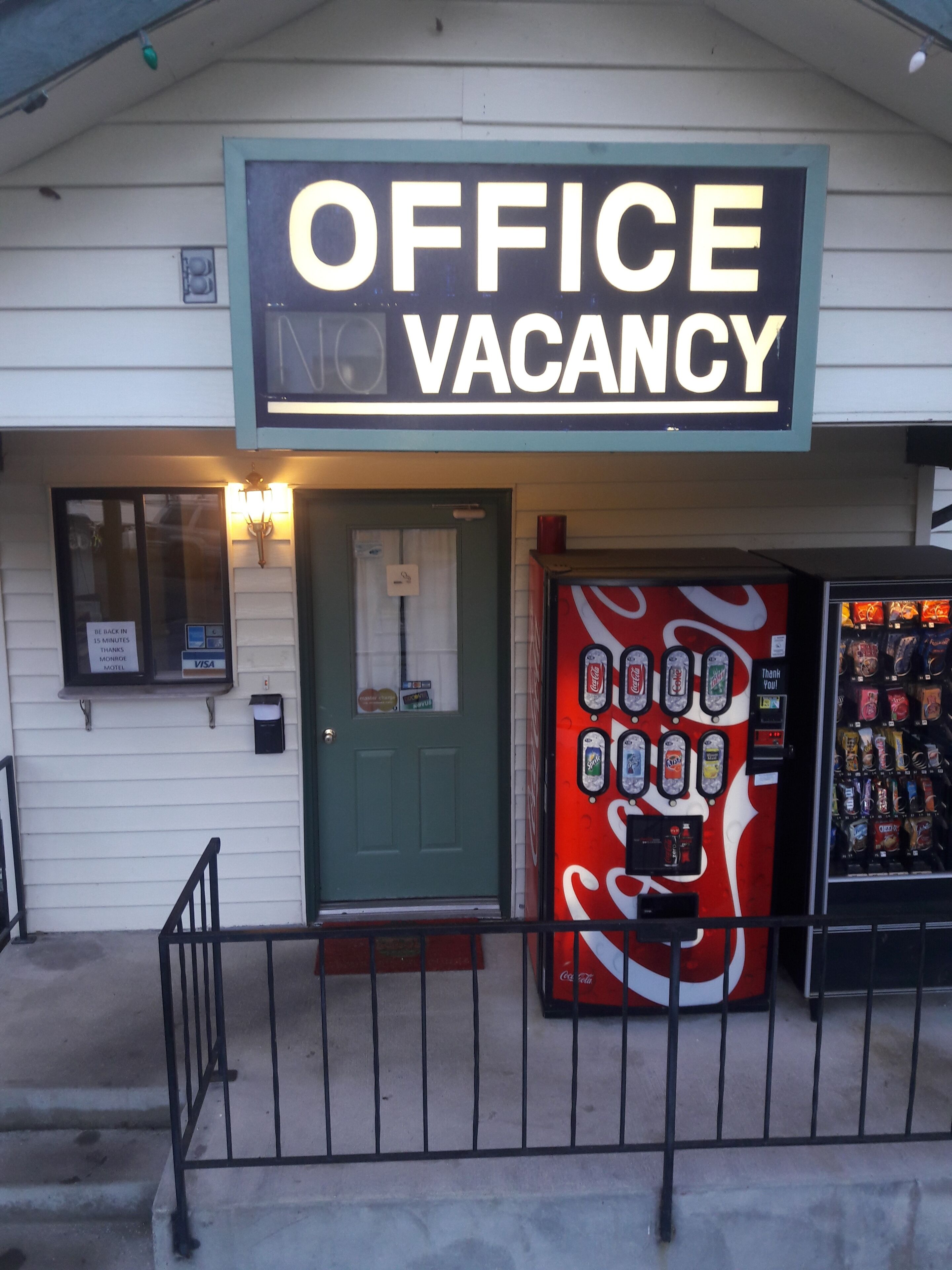 Un edificio con un cartel que dice 'OFFICE VACANCY' y una máquina expendedora de Coca-Cola.