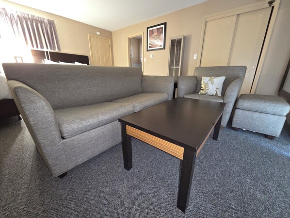 A living room with a grey sofa, a matching armchair, and a dark wooden coffee table. - Monroe Motel Near Seattle Everett WA (Monroe)